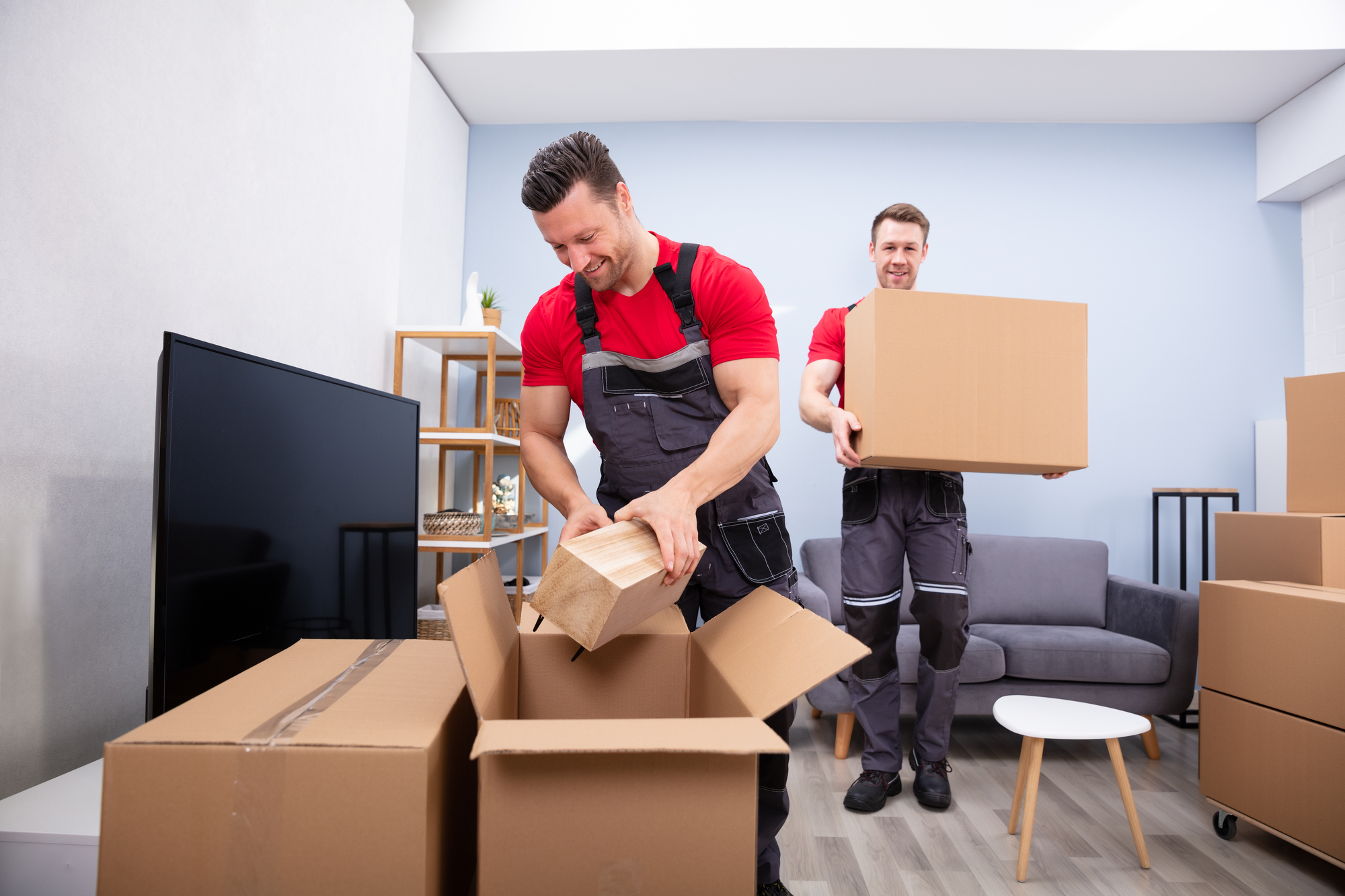 Two Young Movers In Uniform Picking And Putting Products In The Cardboard Boxes